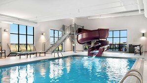 Una piscina interior con tobogán de agua, tumbonas y una escalera que conduce a un nivel superior.