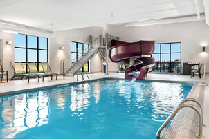 Una piscina interior con tobogán de agua, tumbonas y una escalera que conduce a un nivel superior.