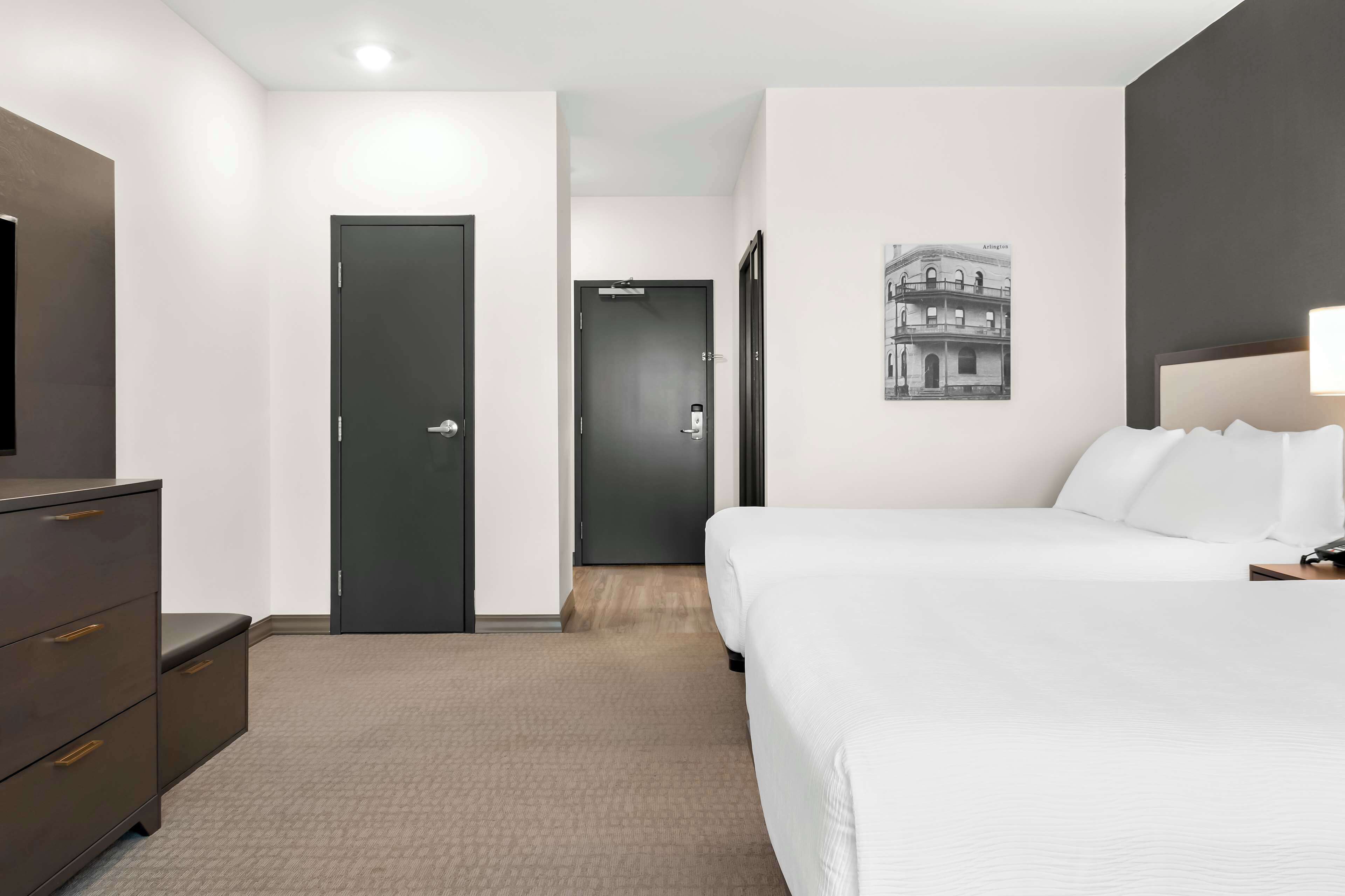 Una habitación de hotel con una cama, un aparador, una puerta y un cuadro colgado en la pared.