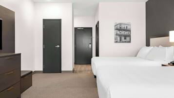 Una habitación de hotel con una cama, un aparador, una puerta y un cuadro colgado en la pared.