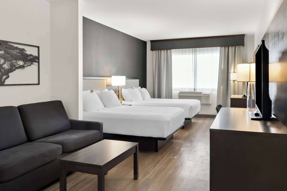 A hotel room with a sofa, two beds, a desk, and a large window with curtains.
