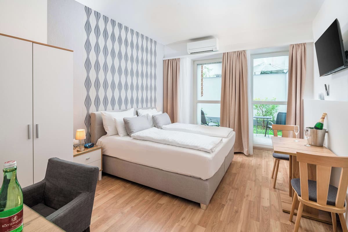 A modern hotel room with a bed, a desk, and a chair. There is a bottle of water on the desk.