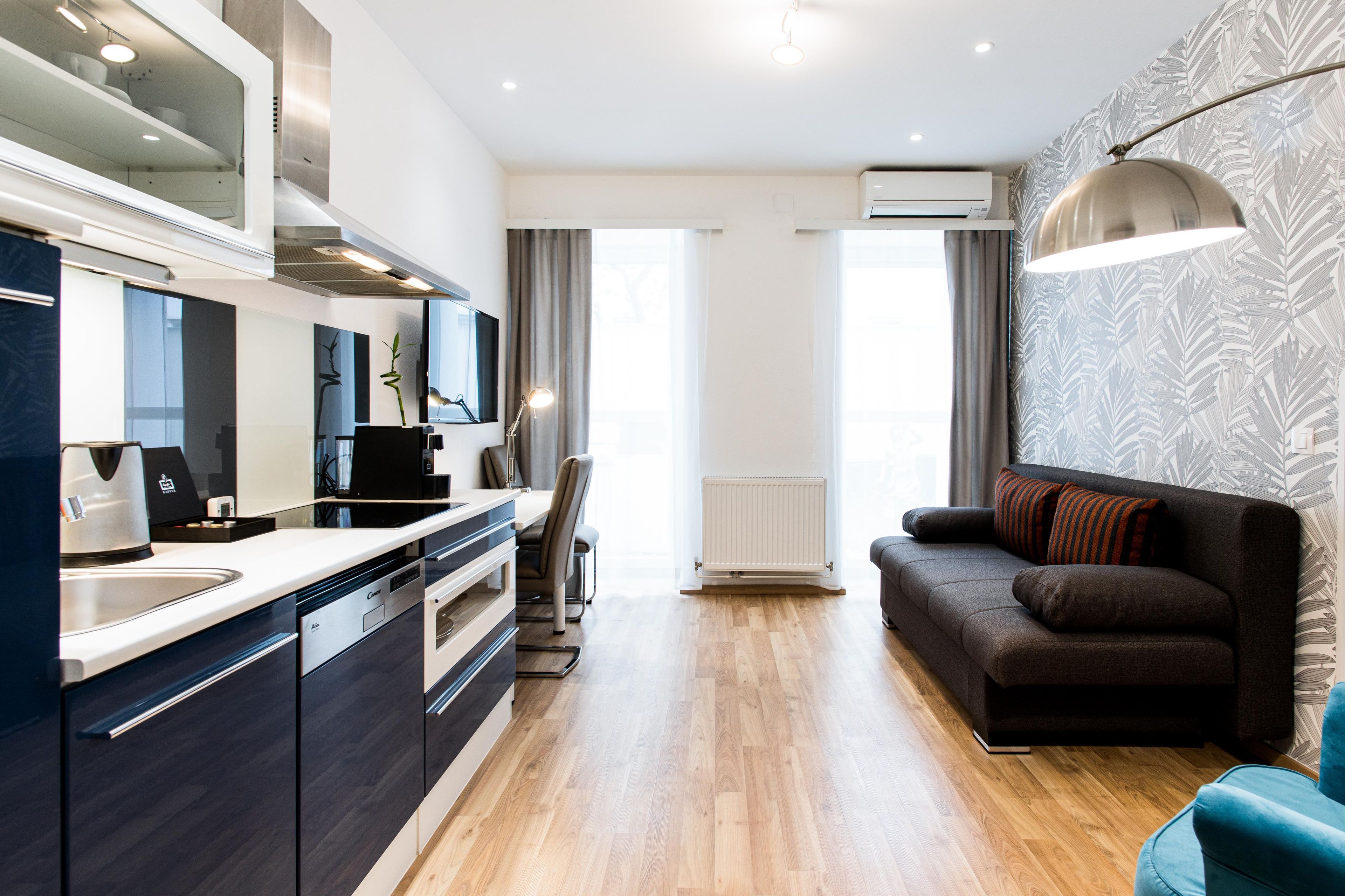 A modern kitchen with a built-in oven, a dining area with a table and chairs, and a living area with a sofa and a lamp.