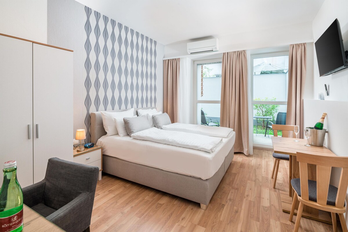 A modern hotel room with a bed, bedside table, lamp, and a bottle of water.