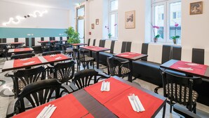 A restaurant with tables set with red placemats and white napkins, black chairs, and potted plants by the windows. - Best Western Plus Celebrity Suites (Vienna)
