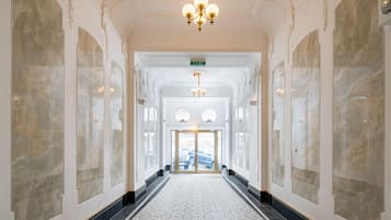 Ein Korridor mit einem gemusterten Boden, einer Chandelier und einer Tür am Ende.