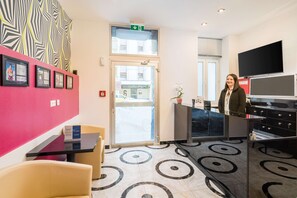 A reception area with a glass door, a reception desk, a TV, and a patterned floor. - Best Western Plus Celebrity Suites (Vienna)