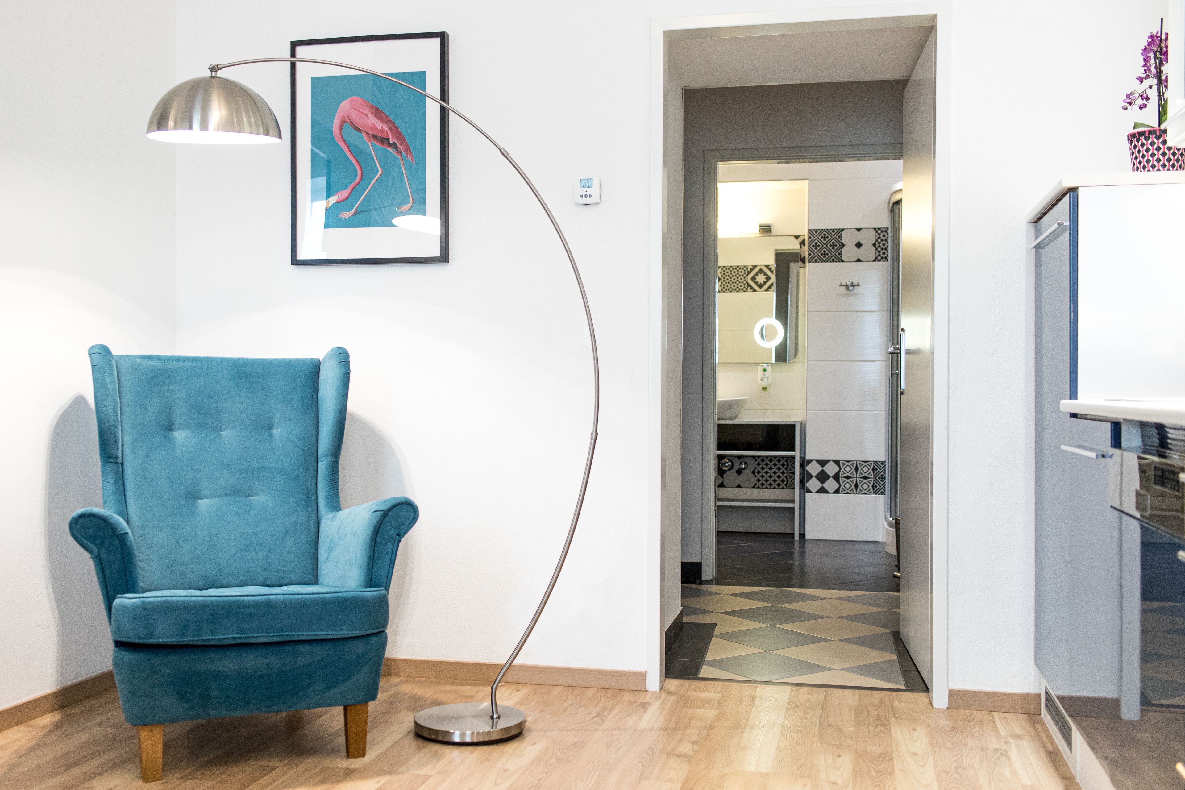 A room with a blue armchair, a floor lamp, and a framed picture on the wall.