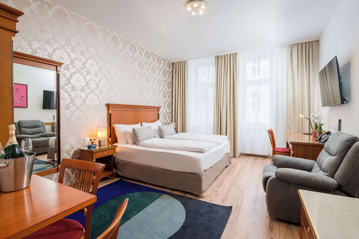 A hotel room with a bed, a desk, a chair, a TV, and a minibar.