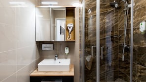 A modern bathroom with a glass-enclosed shower, a white sink, and a wooden vanity. - Best Western Plus Celebrity Suites (Vienna)