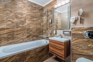 A modern bathroom with a marble wall, a freestanding bathtub, a wooden vanity, and a hairdryer mounted on the wall. - Best Western Plus Celebrity Suites (Vienna)