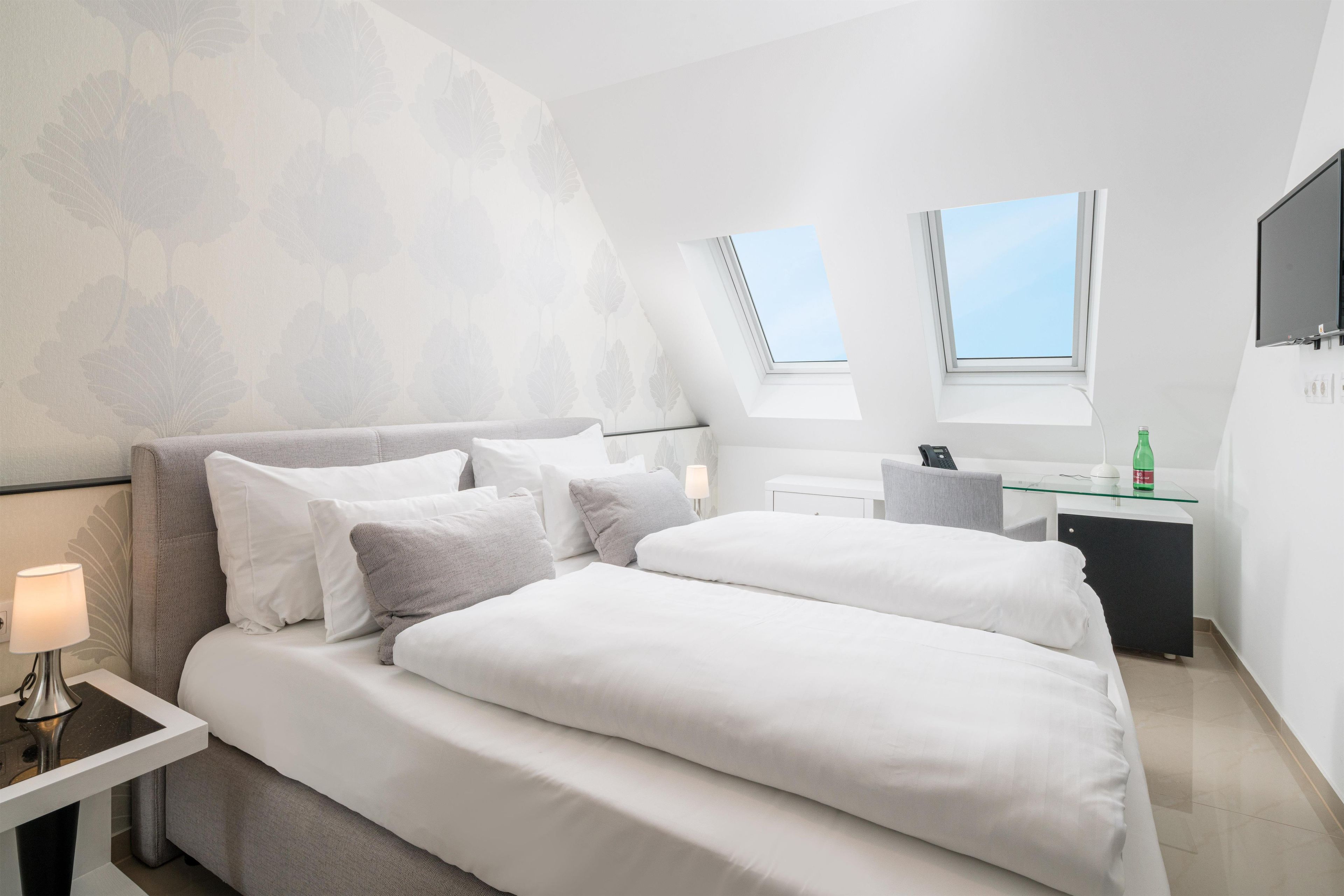 Quarto de hotel moderno com cama, mesas de cabeceira, escrivaninha e janela.
