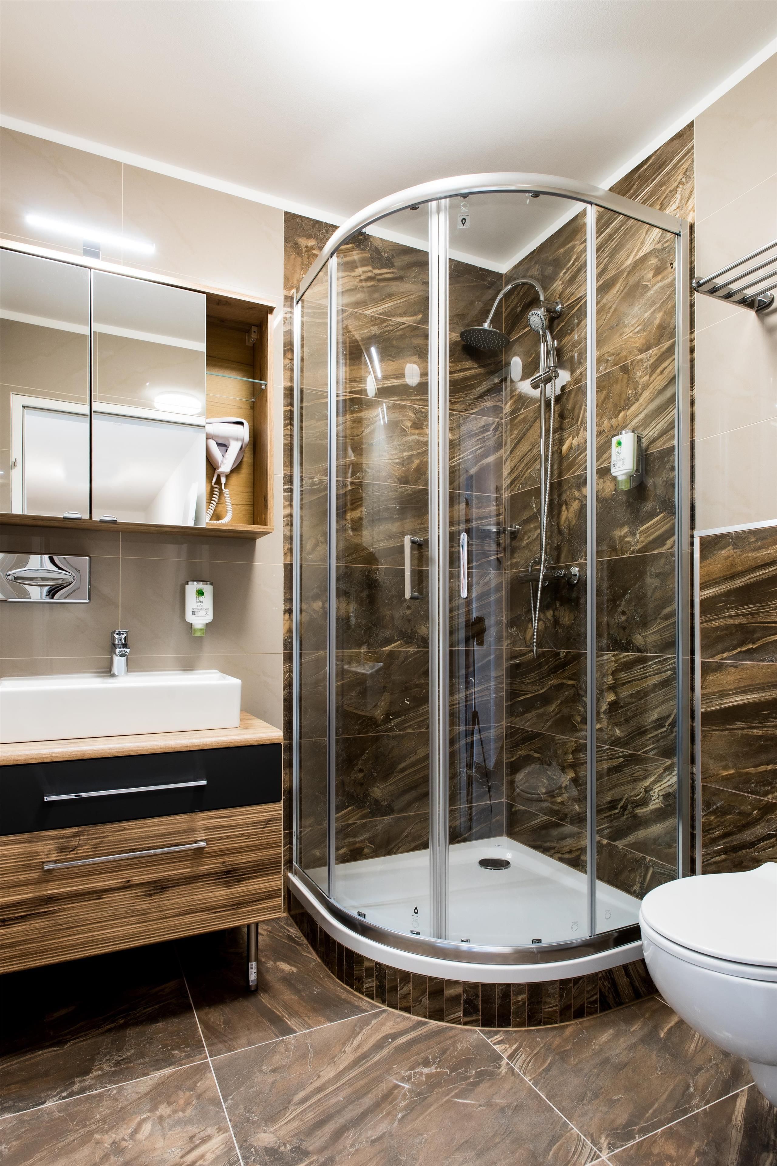Ein modernes Badezimmer mit einer Glaskabine zur Dusche, einem Waschtisch mit Spiegel und einer Toilette.