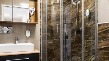 Ein modernes Badezimmer mit einer Glaskabine zur Dusche, einem Waschtisch mit Spiegel und einer Toilette.