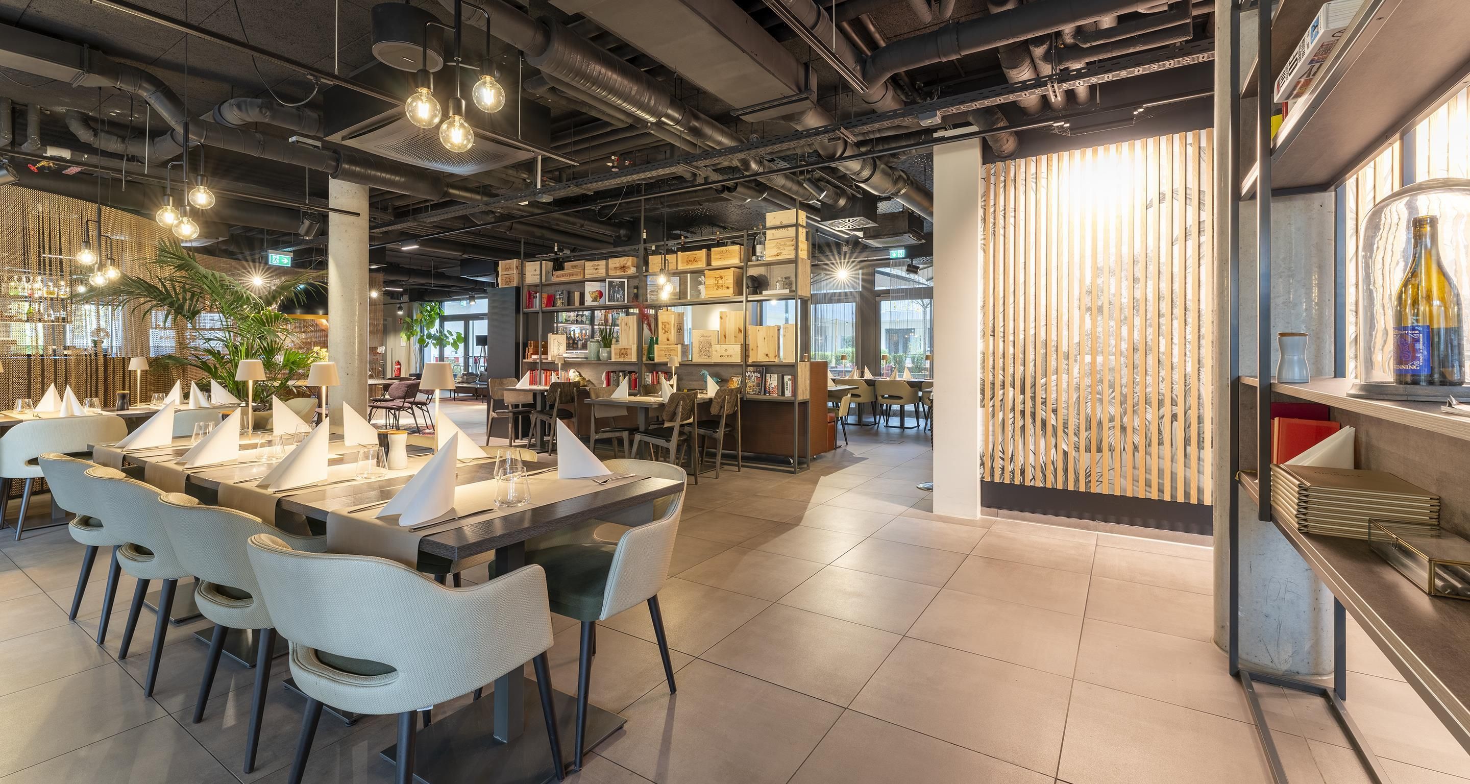 Ein modernes Restaurant mit freiliegenden Lüftungsrohren, Pendelleuchten und verschiedenen Sitzmöglichkeiten.