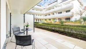 A modern outdoor patio with two black metal chairs and a small round table, a white railing, and a view of a multi-story building with balconies. - Aiden by Best Western Biberach (Biberach an der Riss)