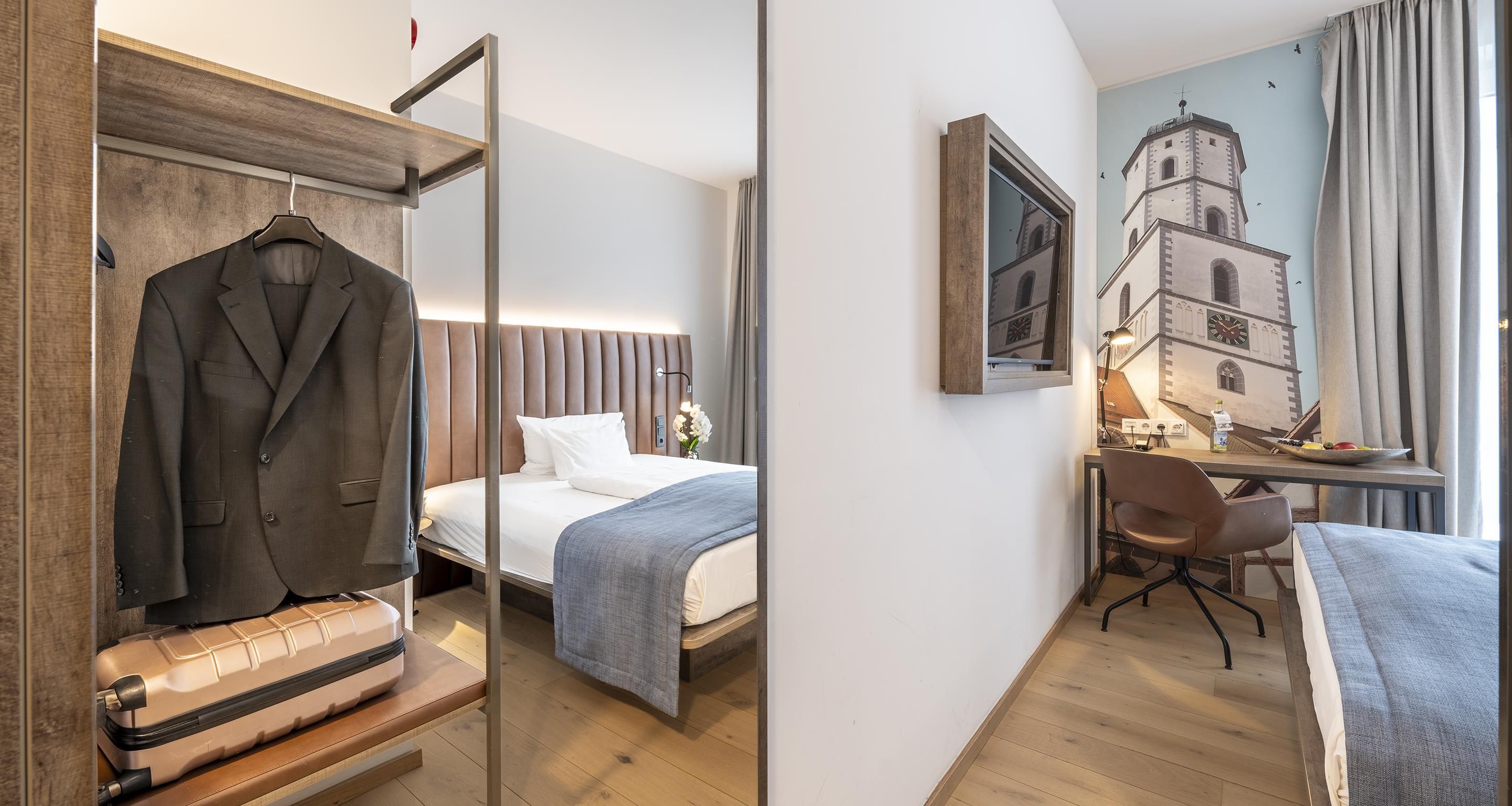 Habitación de hotel con cama, escritorio, silla, perchero y espejo.