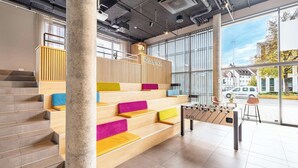 A modern reception area with a wooden reception desk, colorful seating, and a foosball table. - Aiden by Best Western Biberach (Biberach an der Riss)