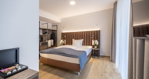 Habitación de hotel moderna con cama, mesita de noche, lámpara y televisor sobre un mueble.
