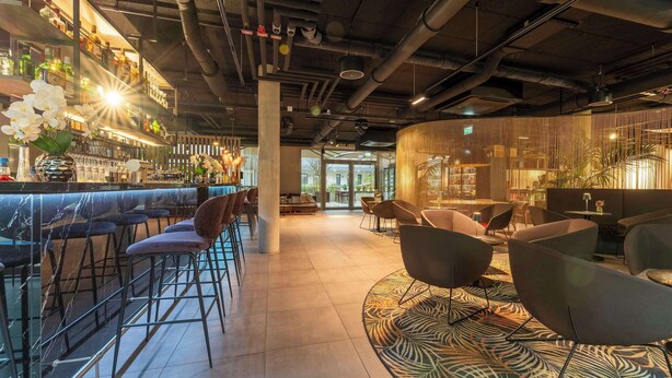 A modern bar area with bar stools, a patterned rug, and a variety of bottles on shelves. - Aiden by Best Western Biberach (Biberach an der Riss)