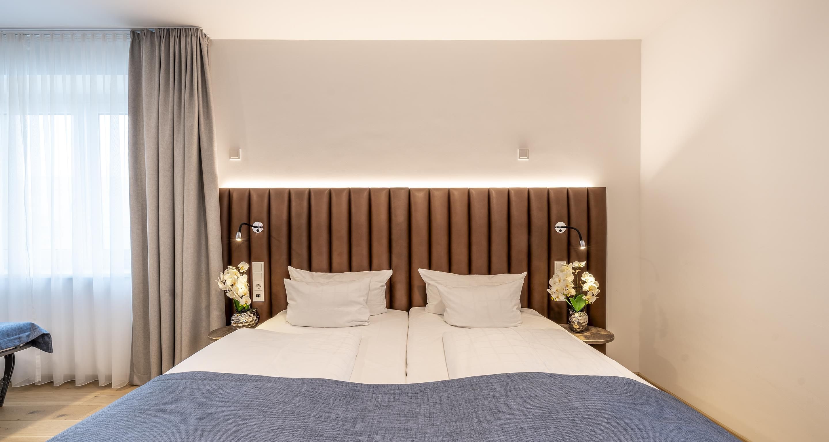 Et moderne hotelværelse med en stor seng, to sengeborde med lamper, et natbord og en stol.
