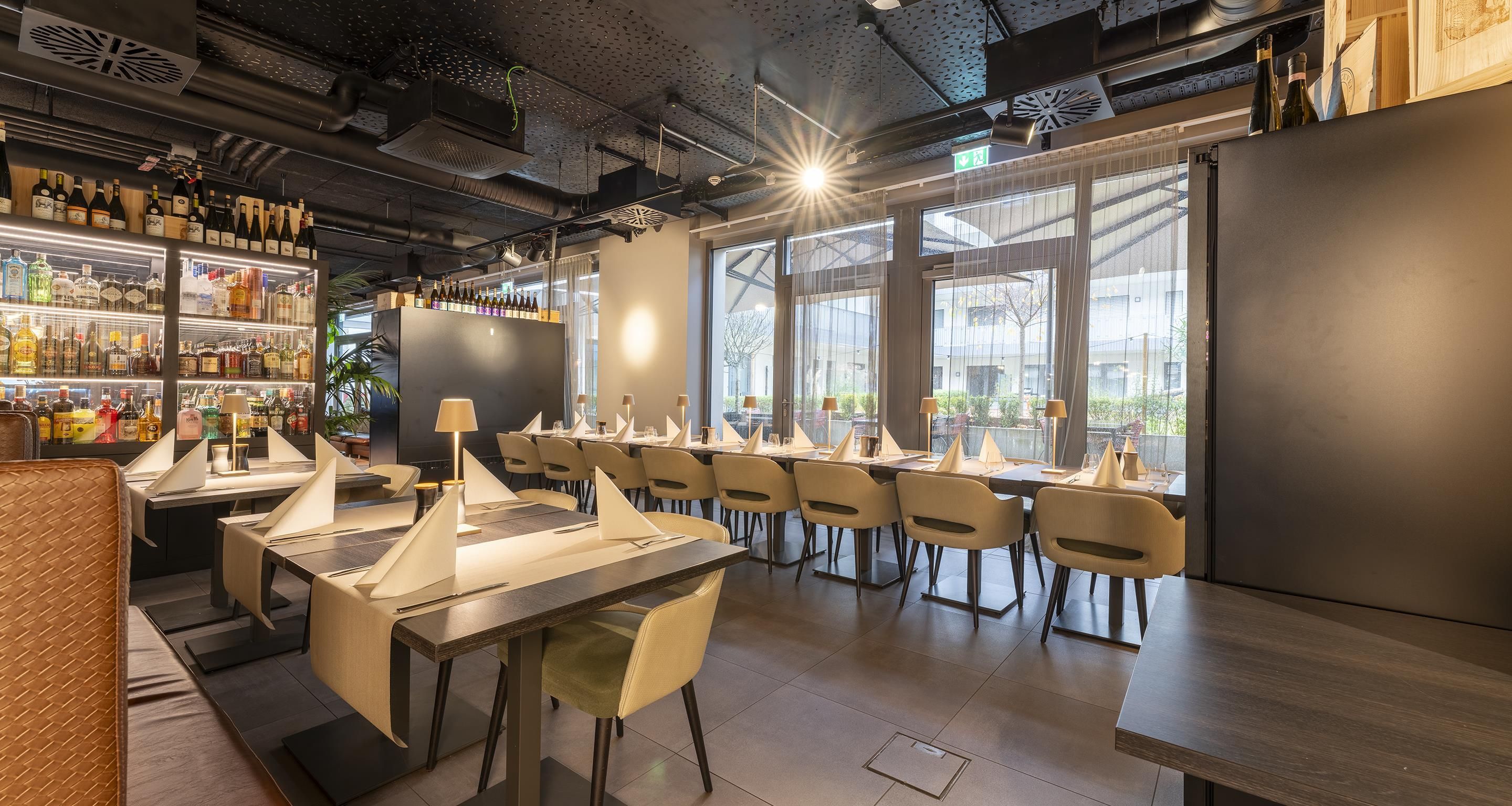 A restaurant interior with tables, chairs, and a bar area with bottles.