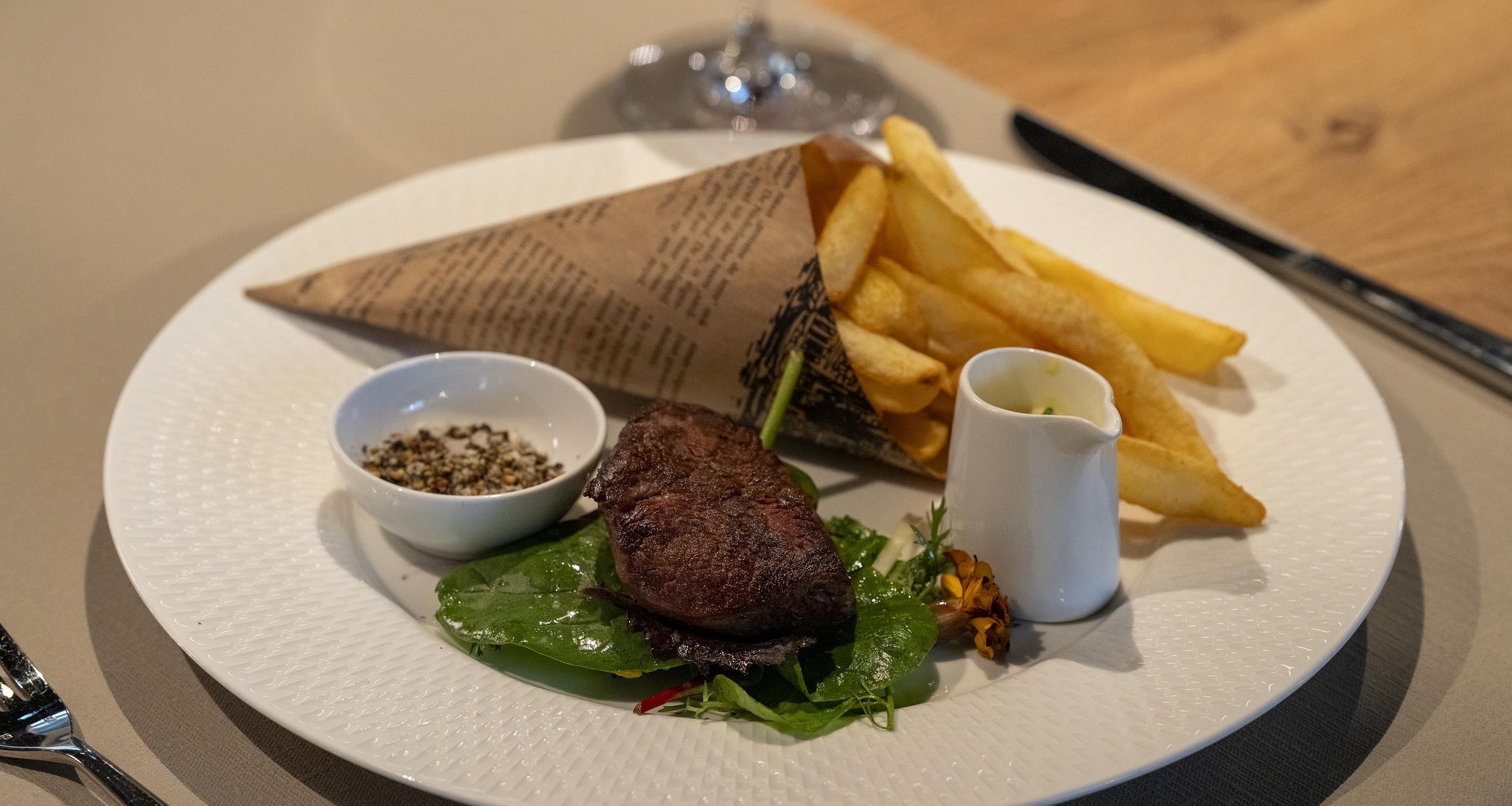 Une assiette avec un hamburger, des frites, un petit bol d’assaisonnement et une tasse de sauce.