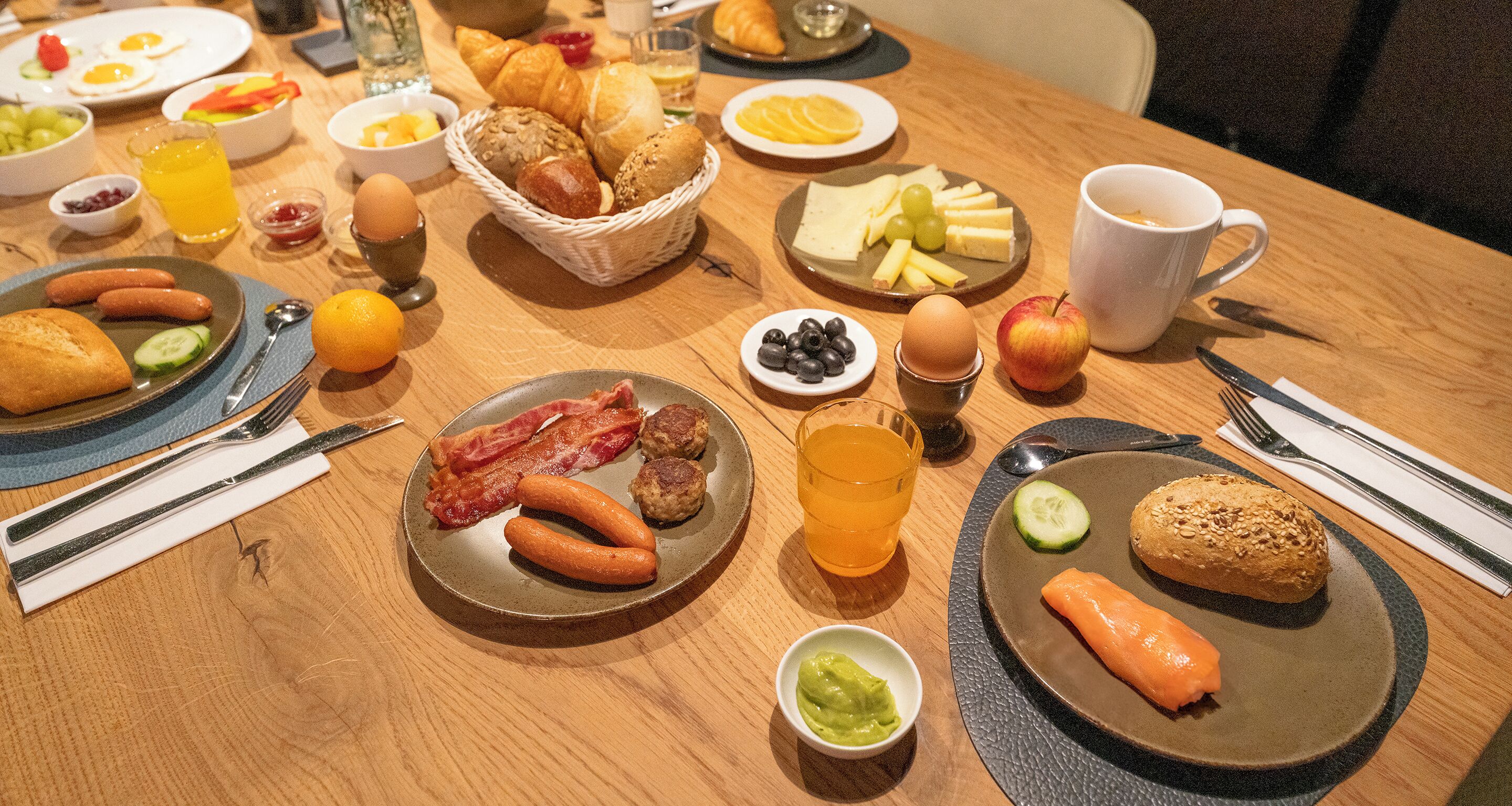 A breakfast table with various food items, plates, and utensils.