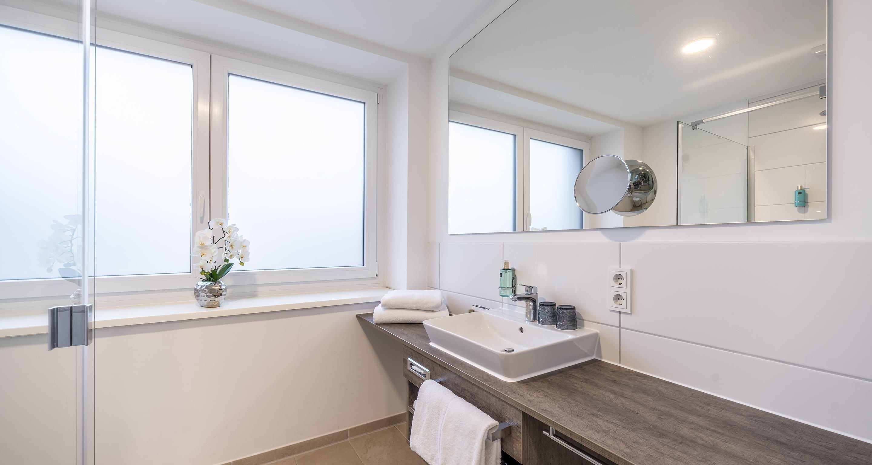 Une salle de bain moderne avec une grande fenêtre, un lavabo blanc et un miroir.