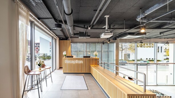 A reception area with a wooden reception desk, a bar seating area, and large windows providing a view of the street outside. - Aiden by Best Western Biberach (Biberach an der Riss)