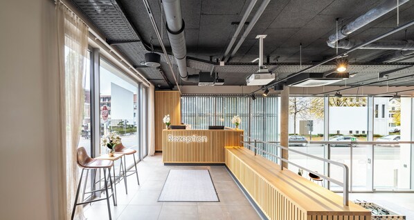 A reception area with a wooden reception desk, a bar seating area, and large windows providing a view of the street outside. - Aiden by Best Western Biberach (Biberach an der Riss)