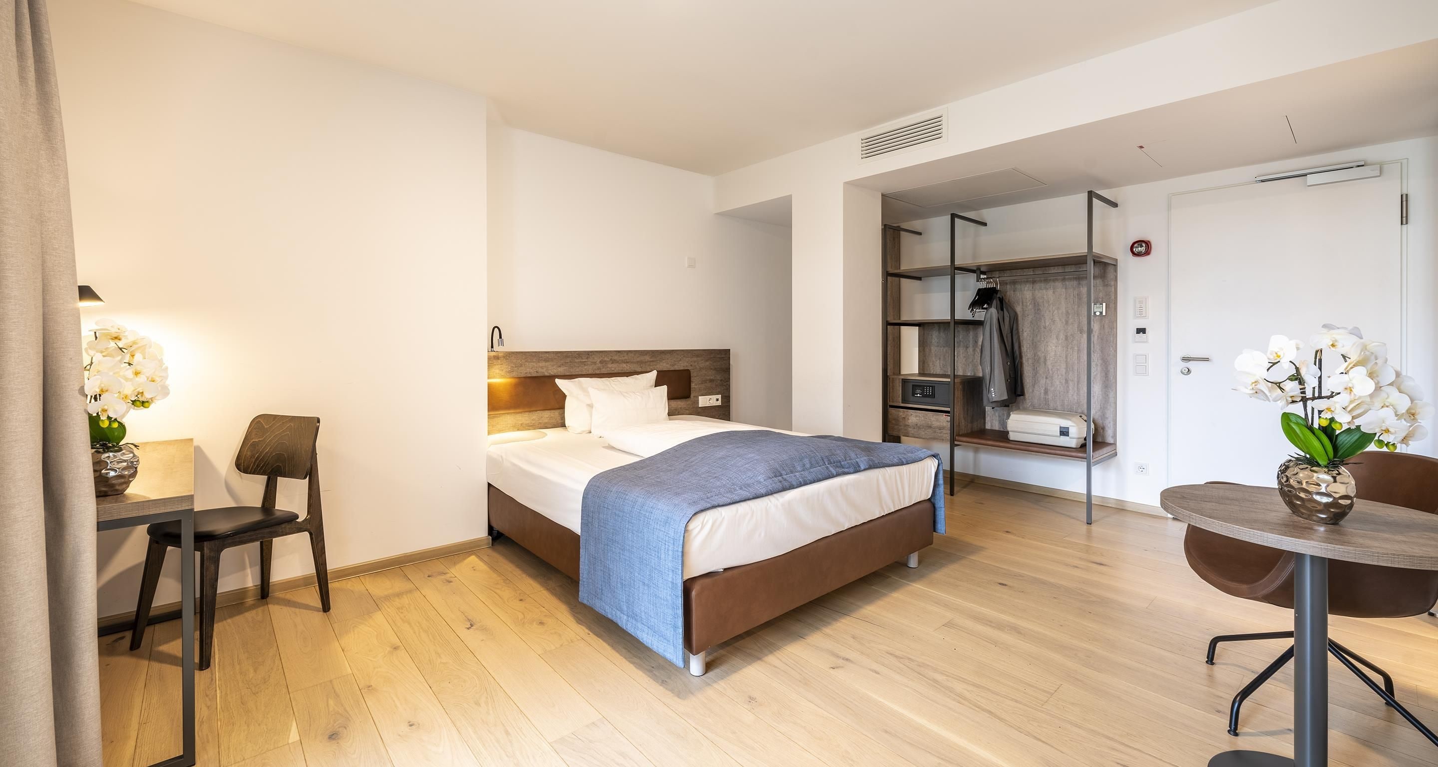 Quarto de hotel com cama, mesa de cabeceira, cadeira, escrivaninha e uma pequena mesa com cadeira.