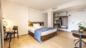 Quarto de hotel com cama, mesa de cabeceira, cadeira, escrivaninha e uma pequena mesa com cadeira.