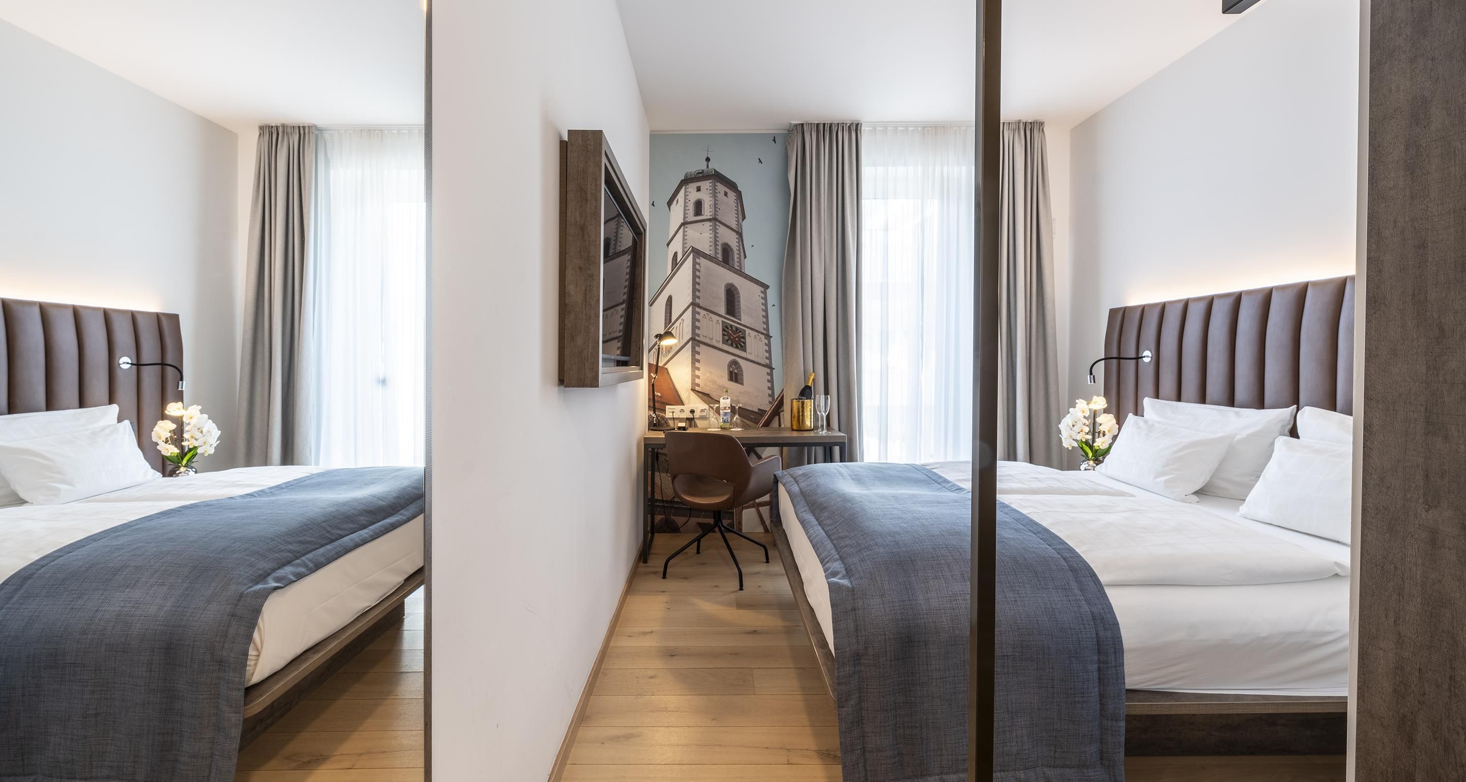 A hotel room with two beds, a desk, and a view of a building through a window.