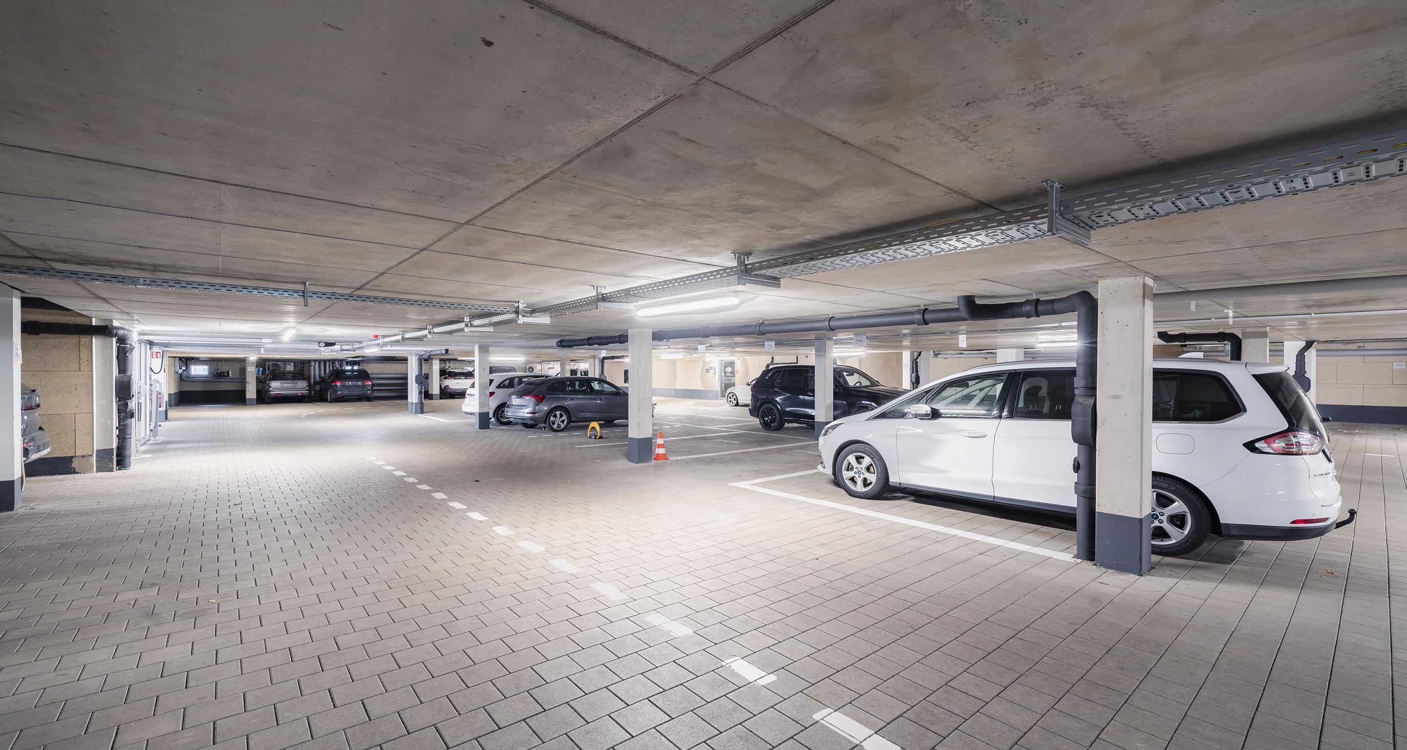 A multi-level underground parking garage with several cars parked, concrete pillars, and a tiled floor.