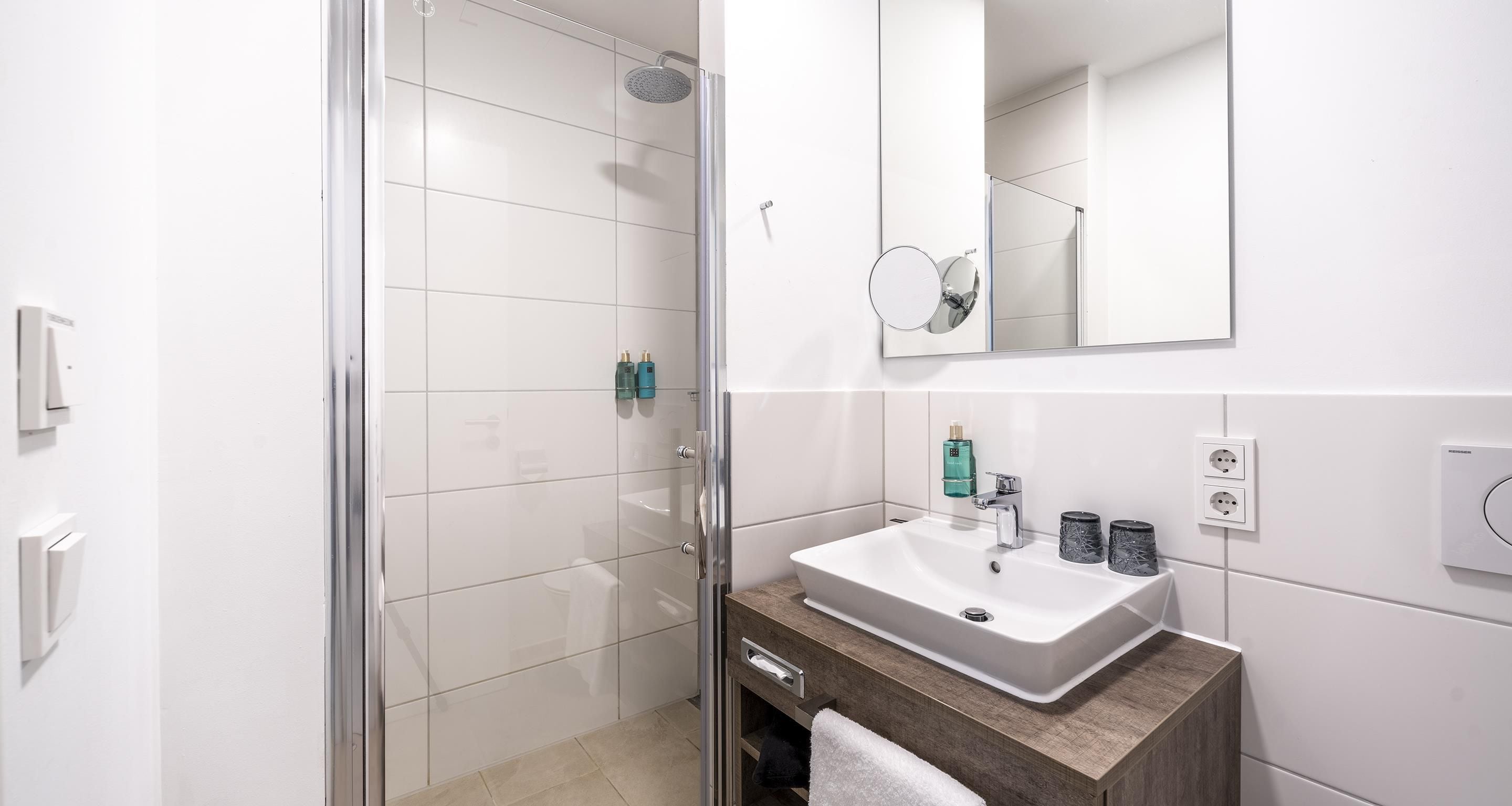Un baño moderno con ducha envuelta en vidrio, un lavamanos blanco con encimera de mármol y un espejo sobre el lavamanos.