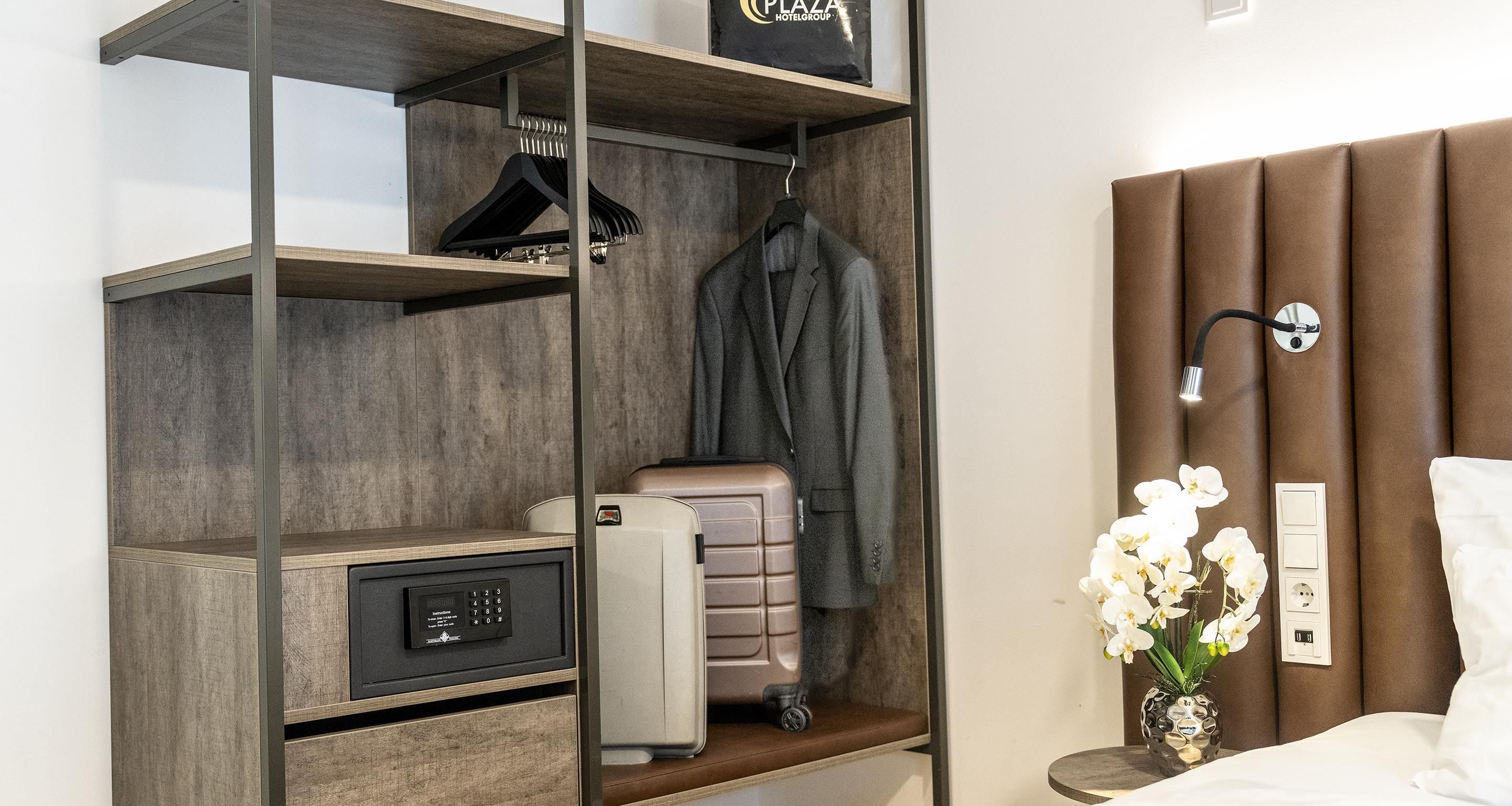 Una habitación de hotel con armario, cama, mesita de noche, lámpara y un jarrón con flores.