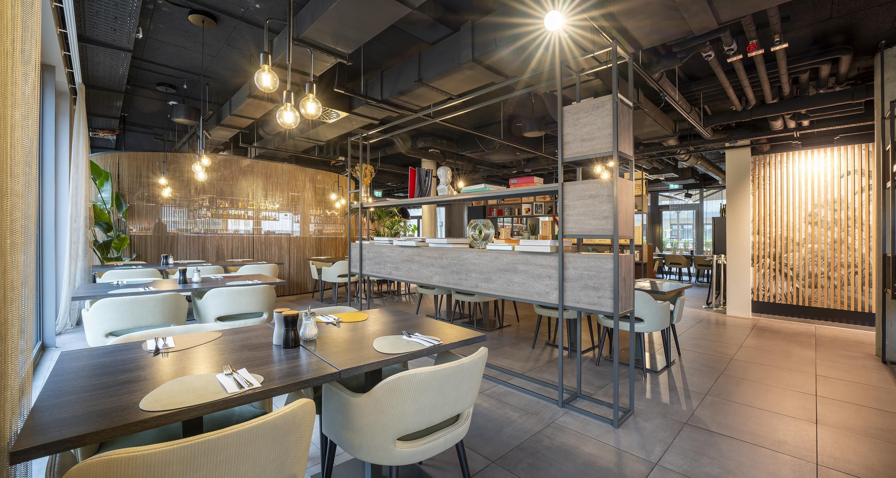 Un intérieur de restaurant moderne avec des plafonds apparents, des luminaires suspendus et un bar central.