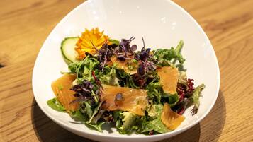 A white bowl containing a salad with various greens, a slice of salmon, and a decorative flower.