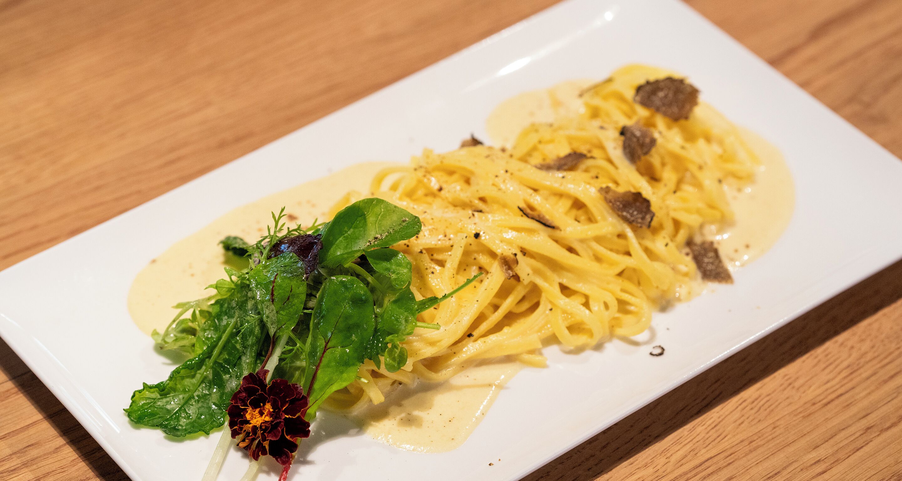 Prato de massa com molho cremoso e carne, decorado com ervas e uma flor.