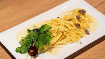 Prato de massa com molho cremoso e carne, decorado com ervas e uma flor.