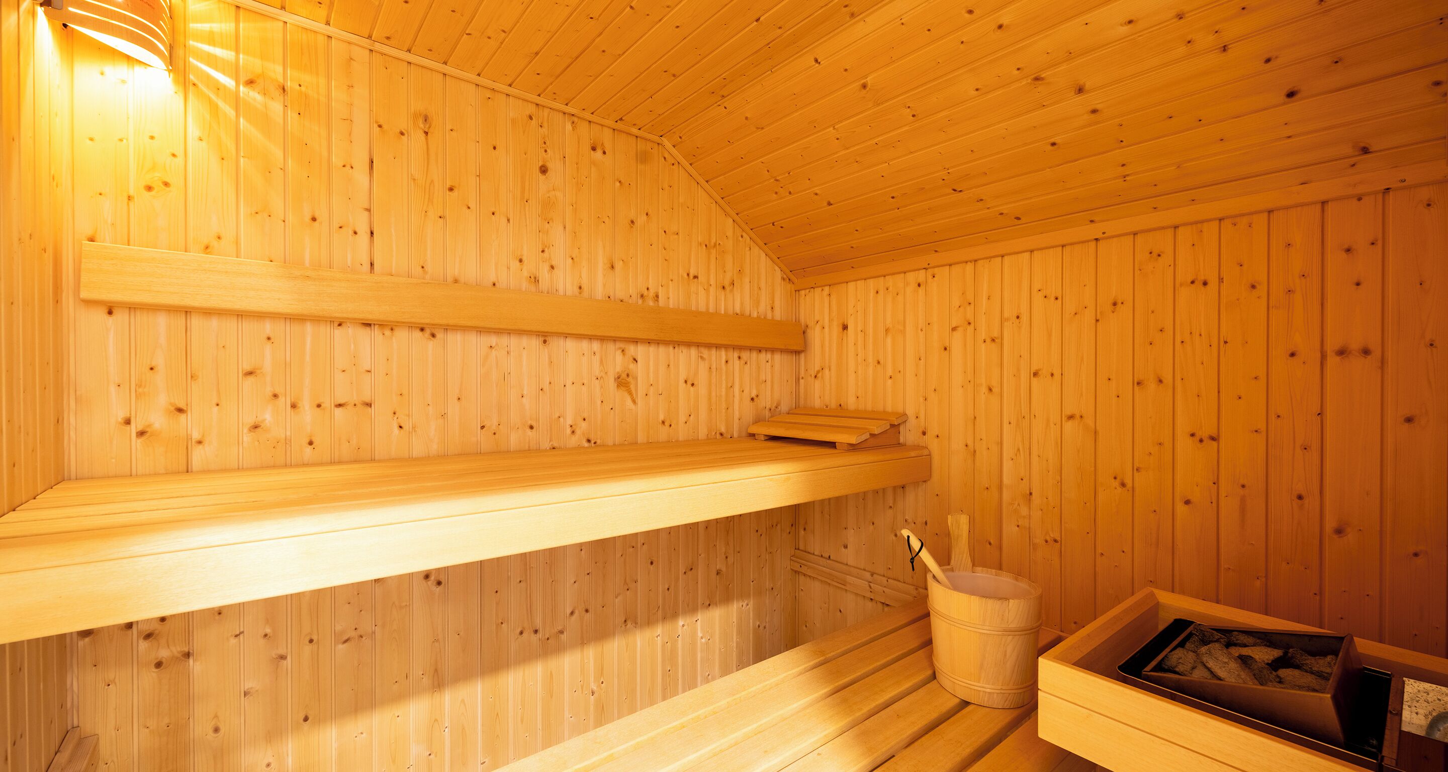 Una sauna de madera con bancos, un cubo y una caja de madera.