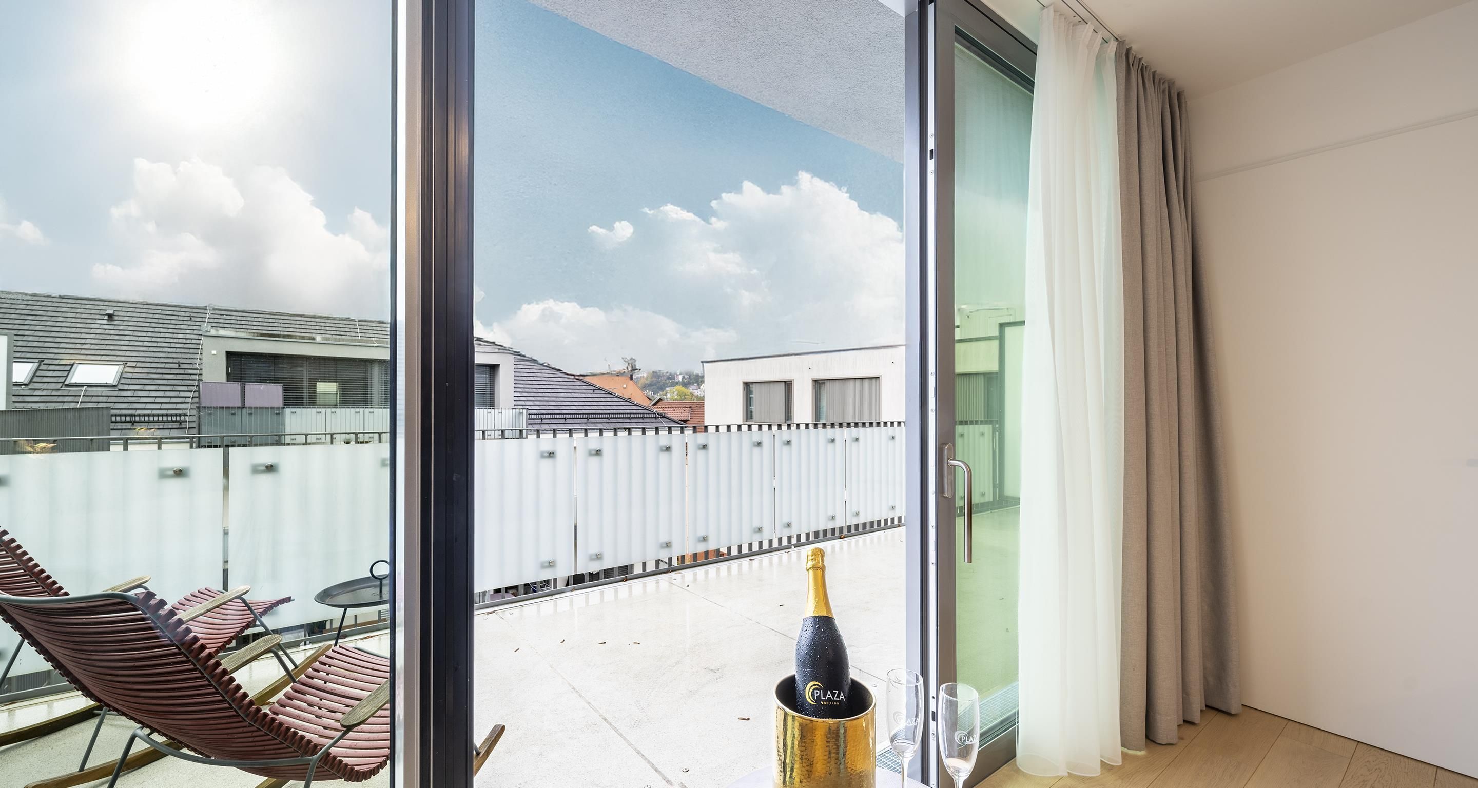 A balcony with a glass door, a bottle of champagne, and a table with chairs.