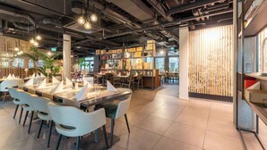 A modern restaurant with a long communal table, white chairs, and hanging pendant lights. - Aiden by Best Western Biberach (Biberach an der Riss)