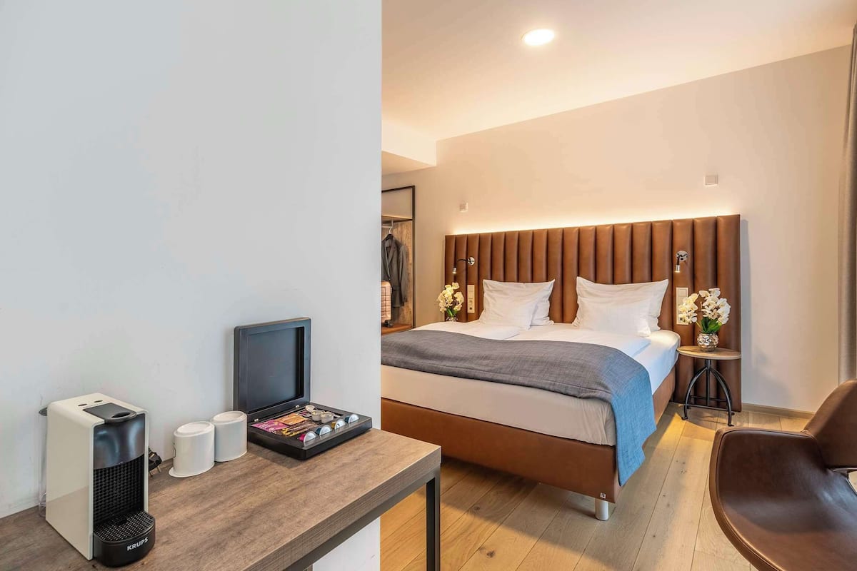 Una habitación de hotel moderna con una cama, mesitas de noche, un escritorio con una cafetera y una silla.