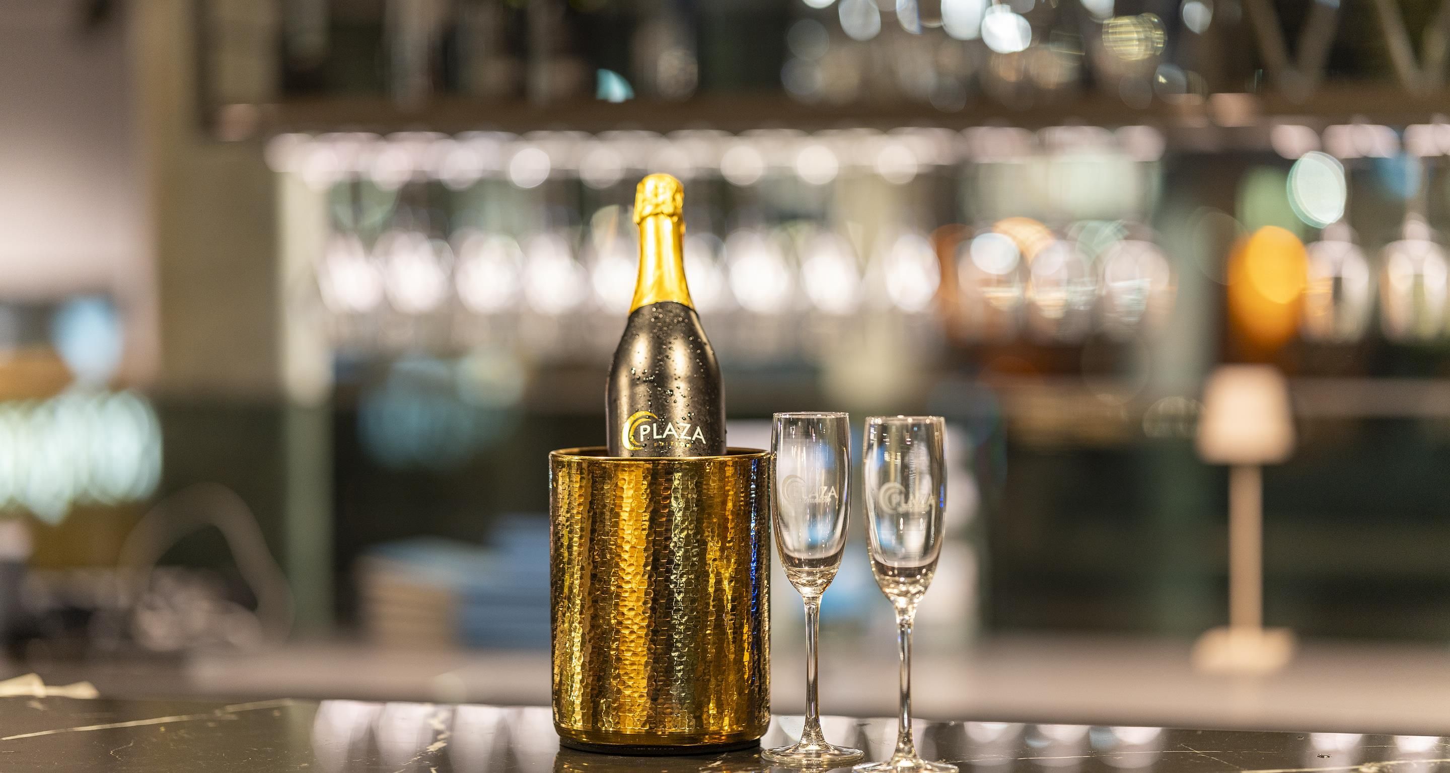 Una botella de champán en un soporte de papel dorado con dos copas a su lado.