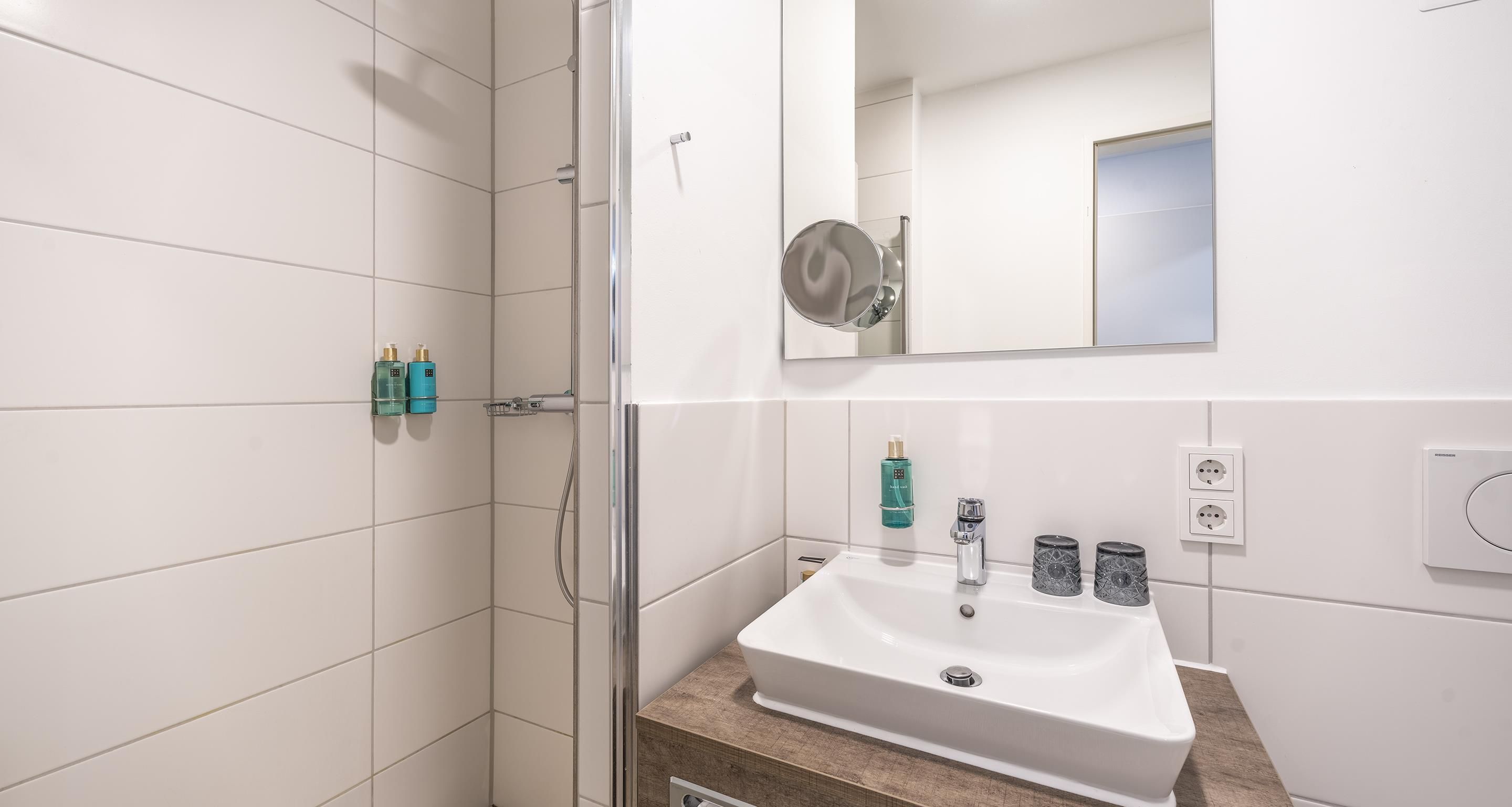 A bathroom with a white sink, a mirror, and two bottles of shampoo on the wall.
