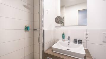 A bathroom with a white sink, a mirror, and two bottles of shampoo on the wall.