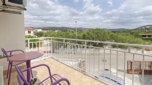 Ein Balkon mit Tisch und Stühlen, einem Geländer und Blick auf eine Straße und Grünflächen.