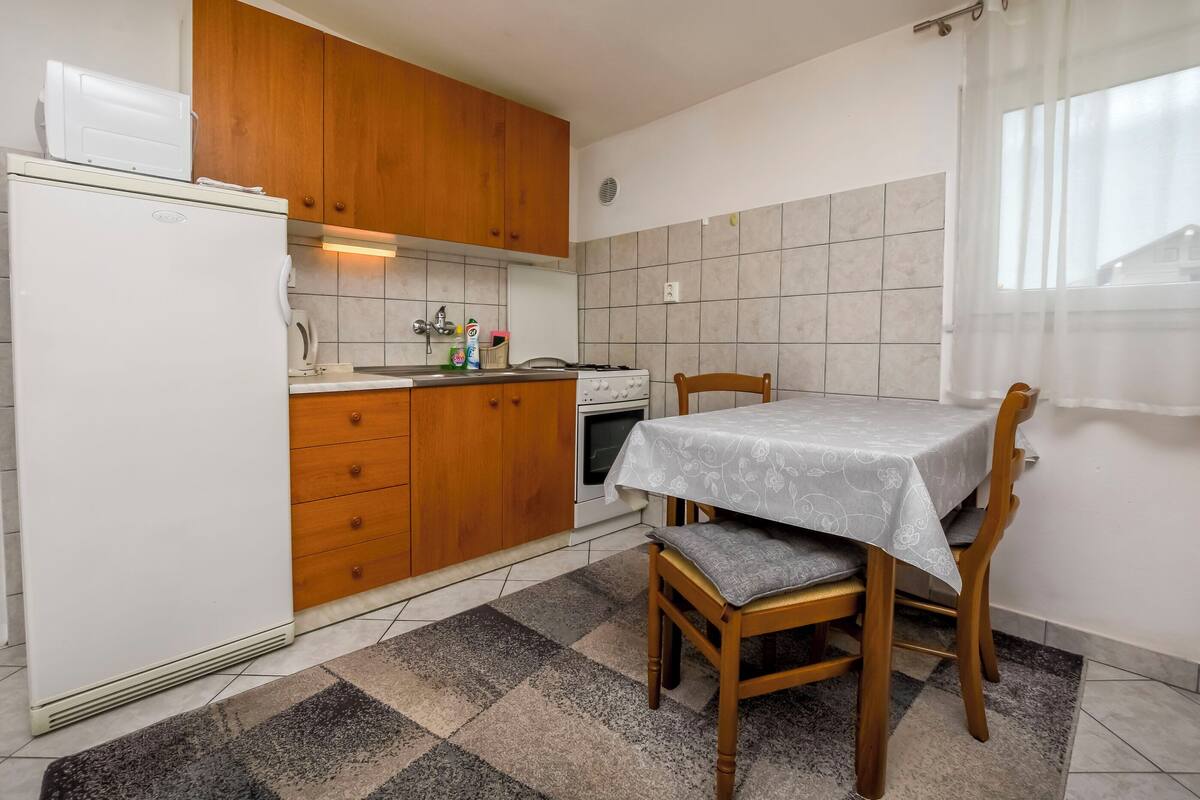 A compact kitchen with wooden cabinets, a white refrigerator, a gas stove, and a dining table with a tablecloth.